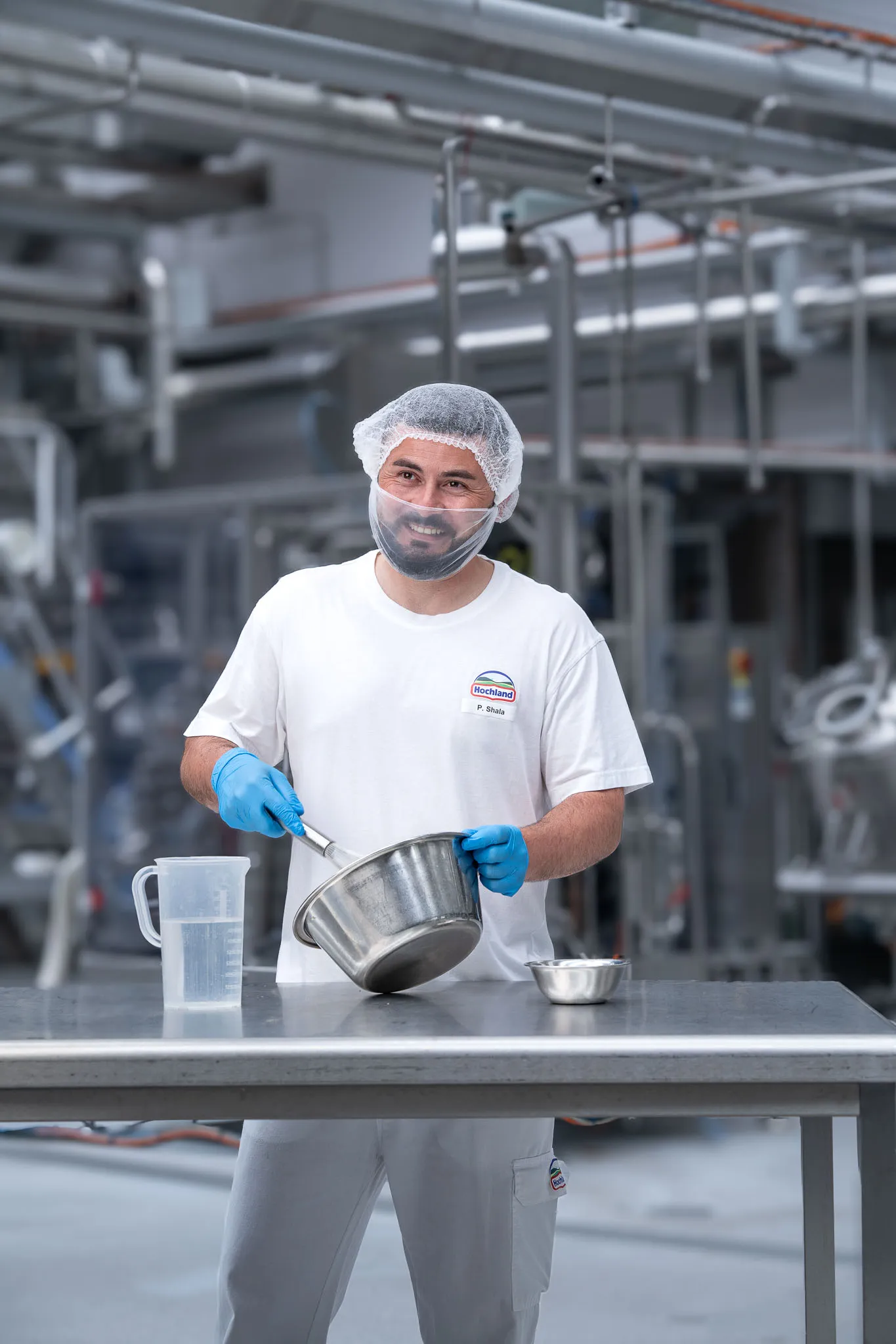 Du siehst einen Hochland-Mitarbeiter in Hygienekleidung, der in der Produktion Zutaten abwiegt und mischt.