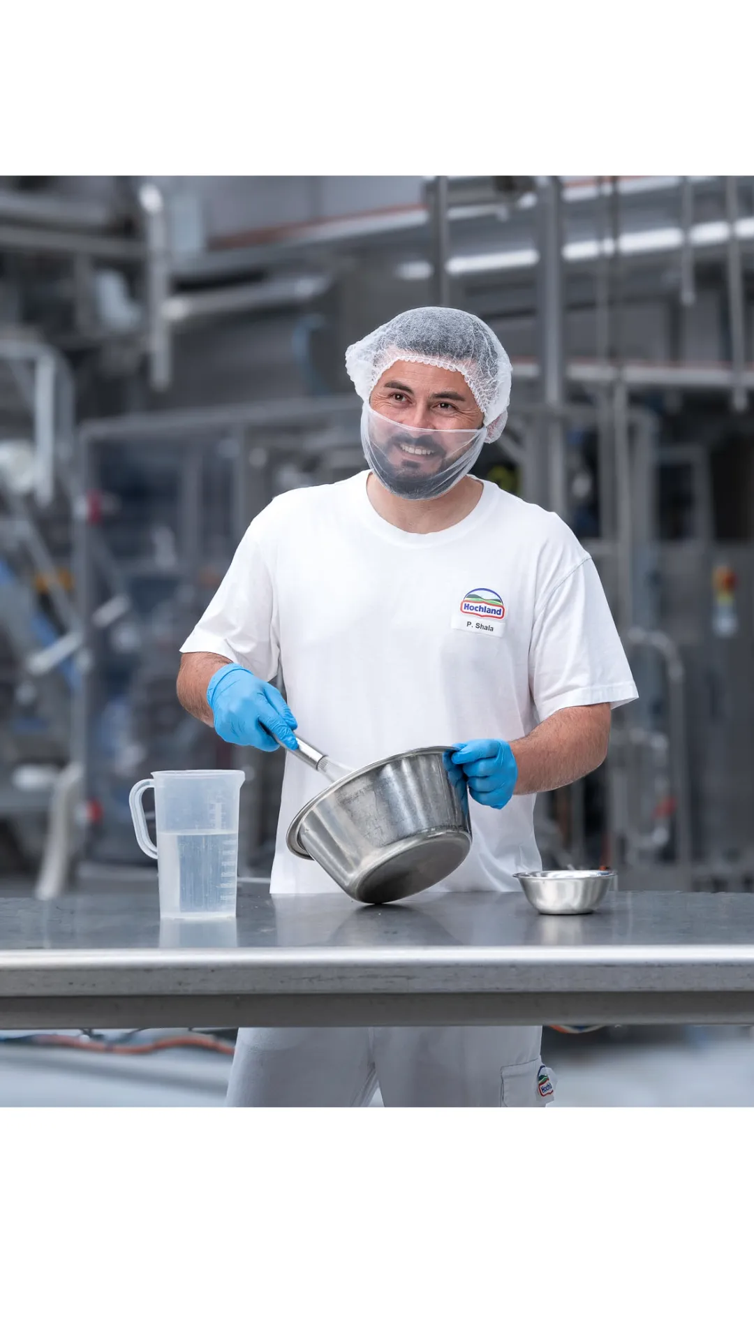 Ein Mitarbeiter mit Bart, Haarnetz und Handschuhen arbeitet lächelnd in der Lebensmittelproduktion.
