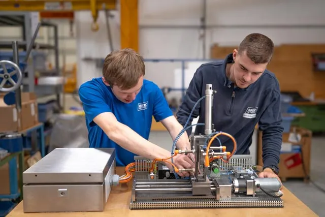 Zwei junge Männer arbeiten gemeinsam an einer technischen Maschine in einer Werkstatt bei Hochland.