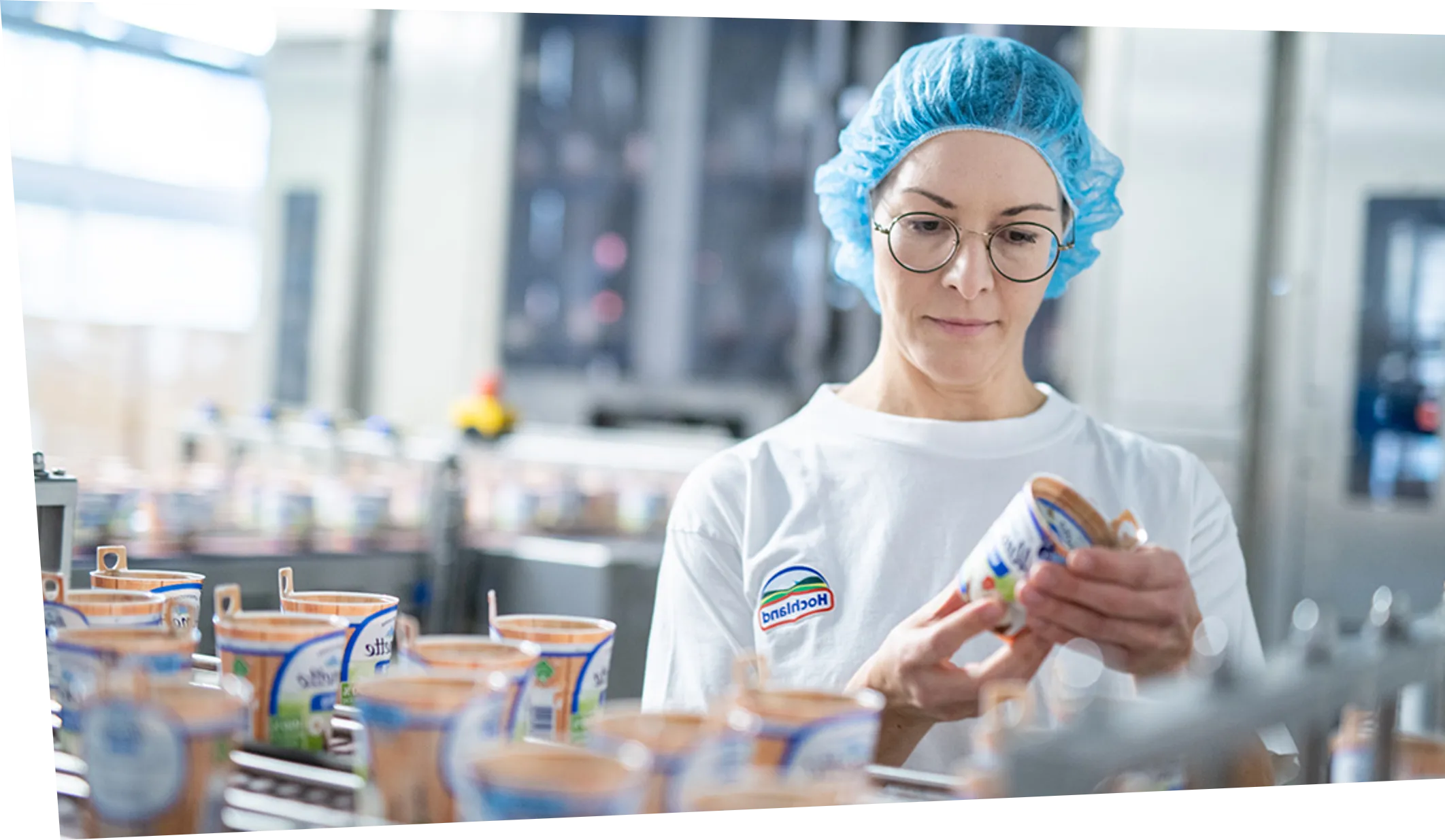 Mitarbeiterin prüft im Hochland-Werk ein Lebensmittelprodukt in der Produktion, um Qualität sicherzustellen.