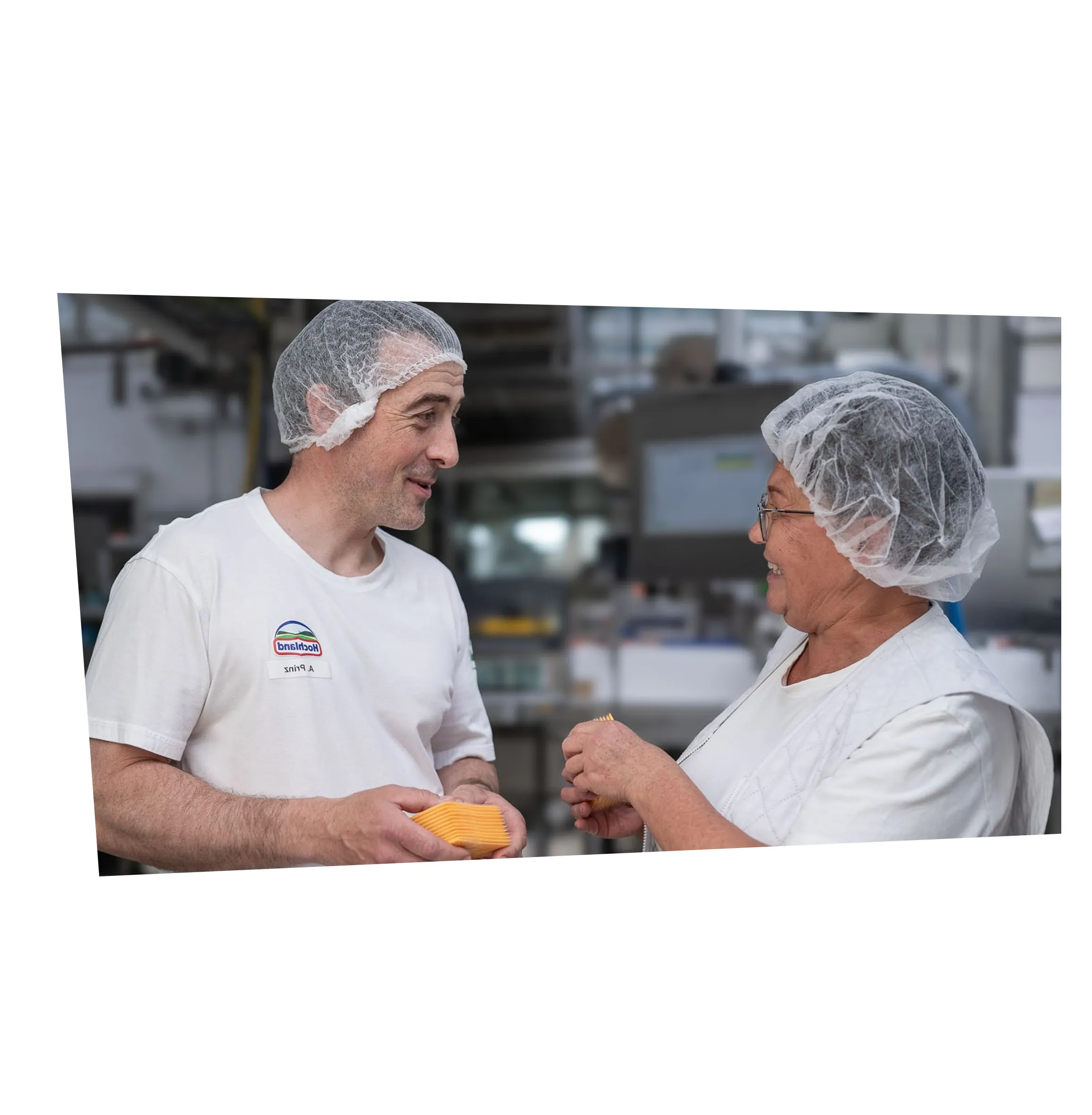 Zwei Hochland-Mitarbeitende im Gespräch in der Produktion, beide tragen Hygienekleidung und lächeln sich an.