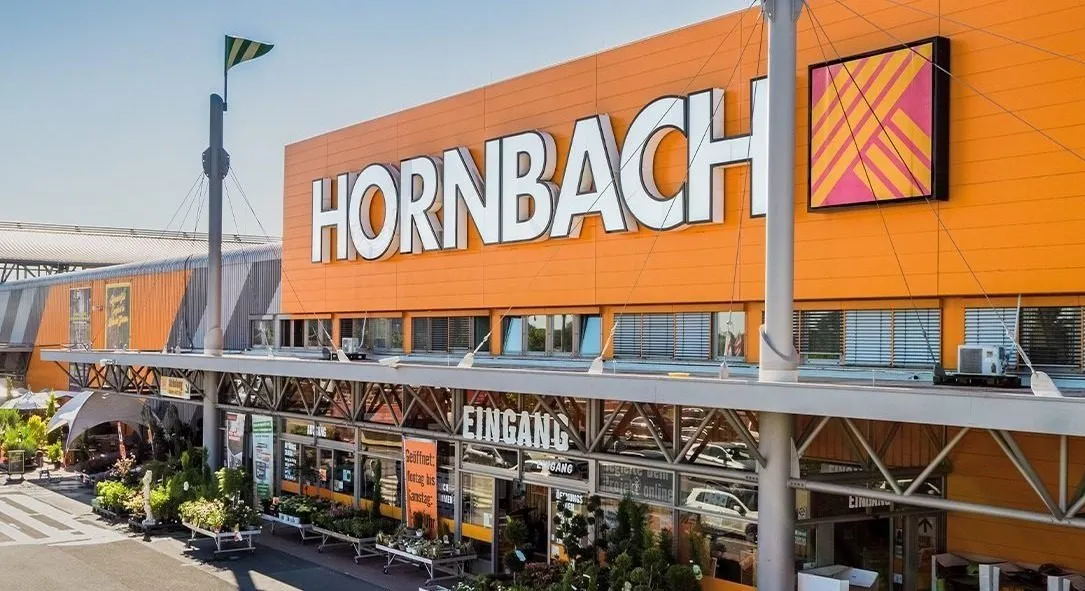 Außenansicht eines HORNBACH Baumarkts mit großem Logo über dem Eingang, Pflanzen im Vordergrund.