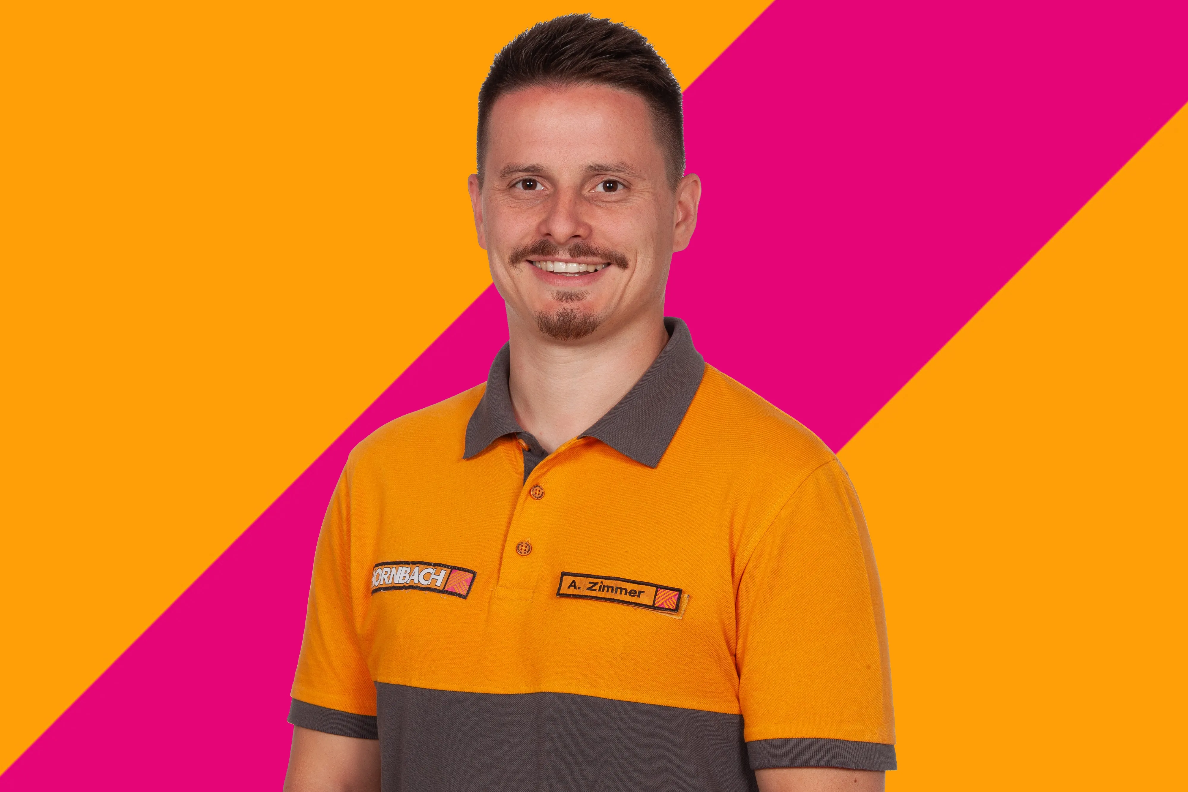 Der Mitarbeiter Andreas Zimmer von HORNBACH Baumarkt AG in orange-grauer Uniform lächelt vor einem bunten Hintergrund.