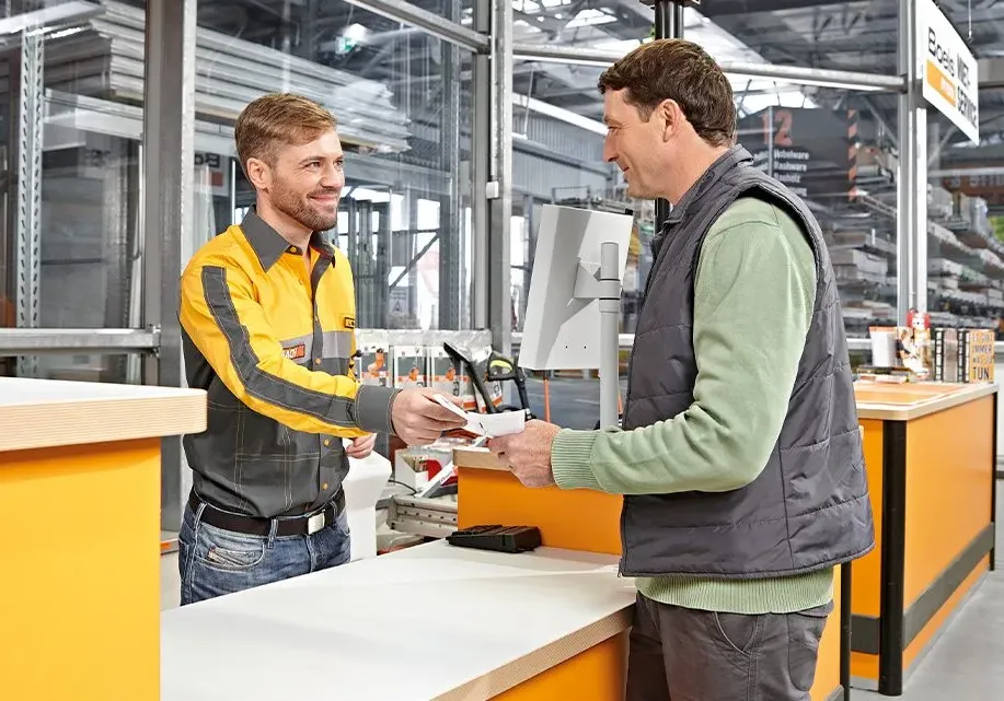 Un employé de HORNBACH sourit en aidant un client à une caisse dans le magasin.