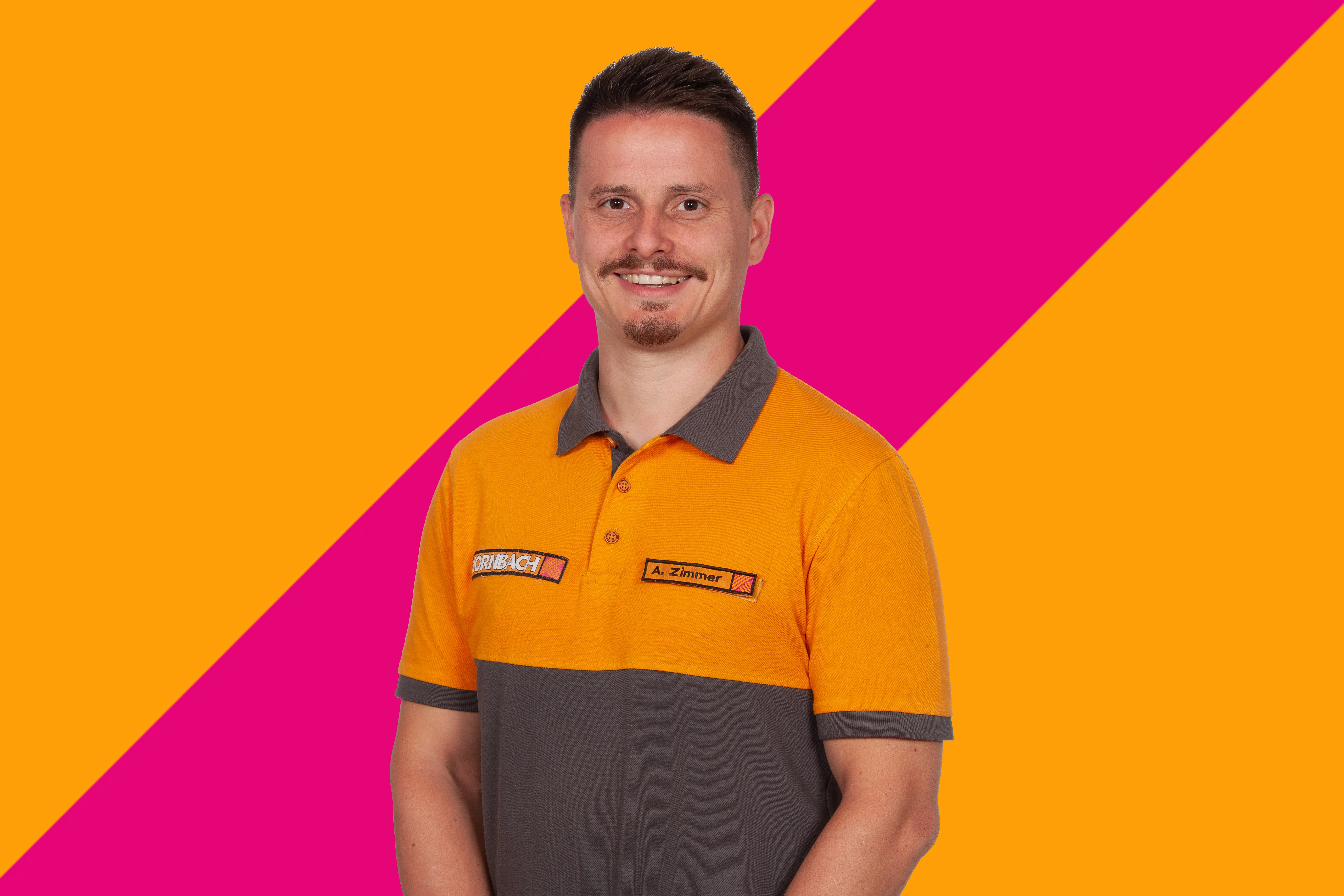 L'employé Andreas Zimmer de HORNBACH souriant, portant un polo orange et gris, sur fond coloré.
