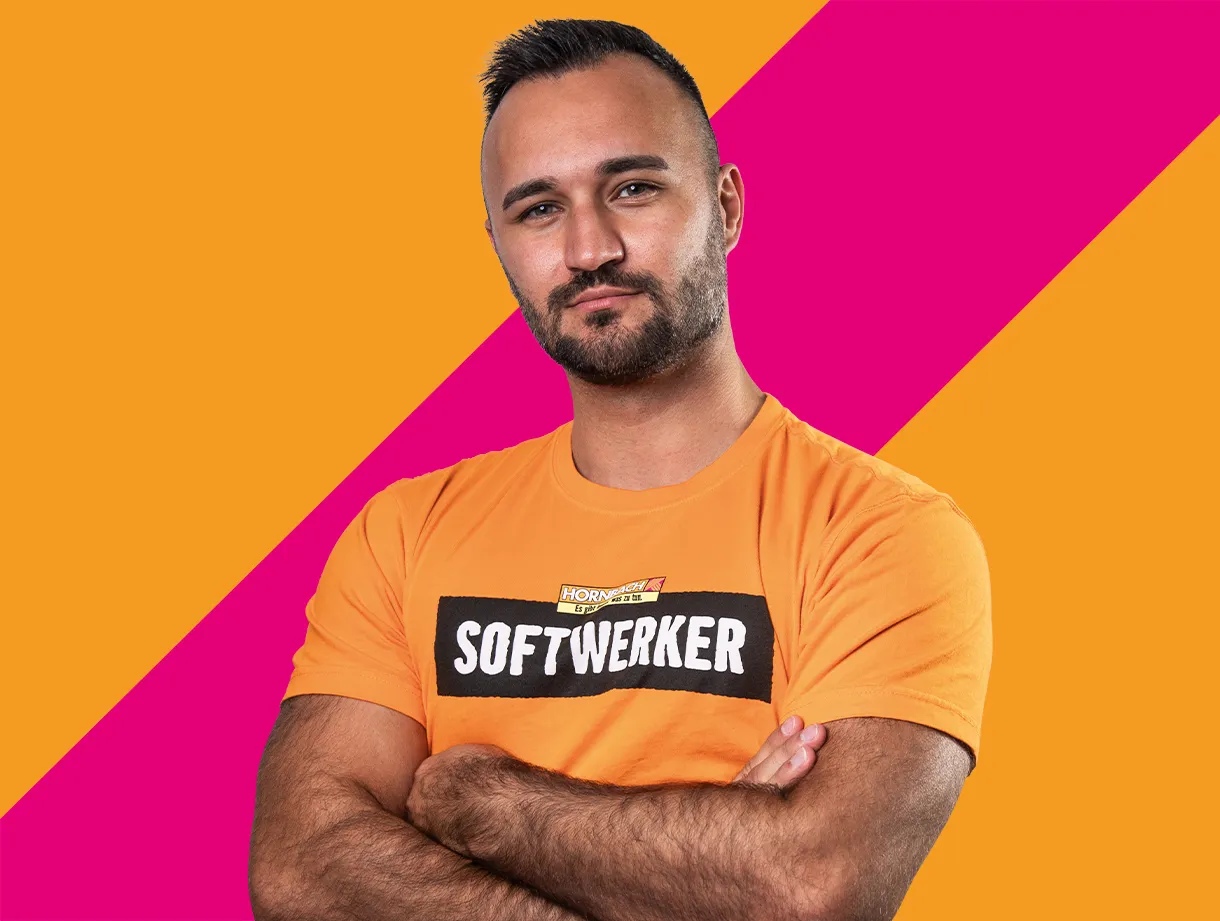 Ein Mann in einem orangefarbenen T-Shirt mit der Aufschrift "SOFTWERKER" vor einem bunten Hintergrund.