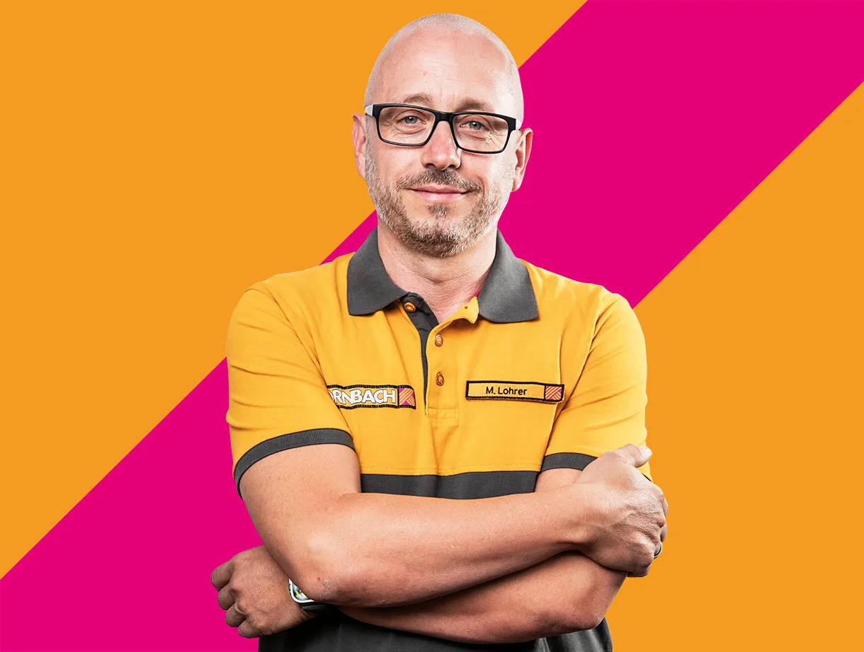 Ein Mitarbeiter von HORNBACH in orange-grauer Arbeitskleidung vor einem farbenfrohen Hintergrund.