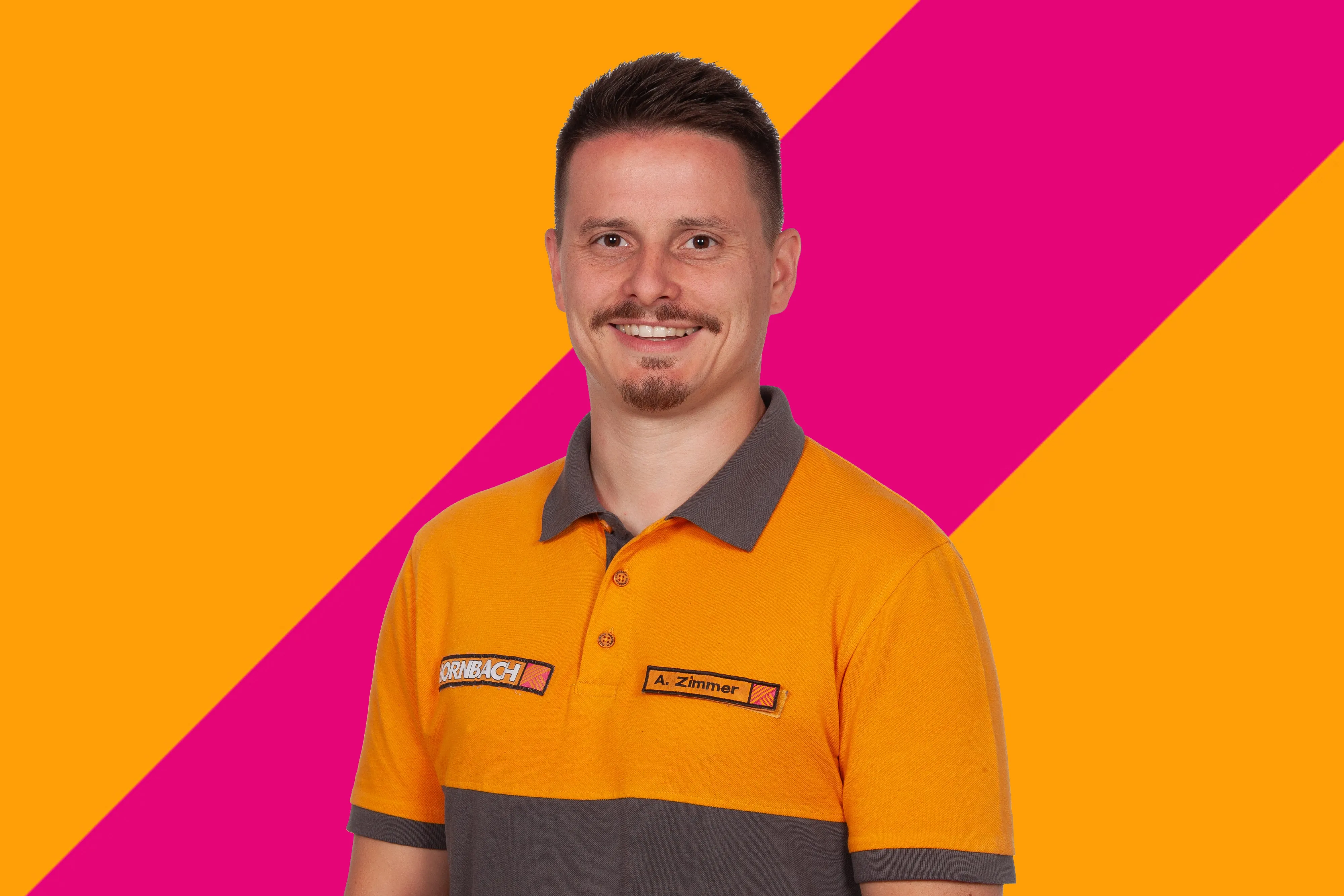L'employé Andreas Zimmer de HORNBACH souriant, portant un polo orange et gris, sur fond coloré.