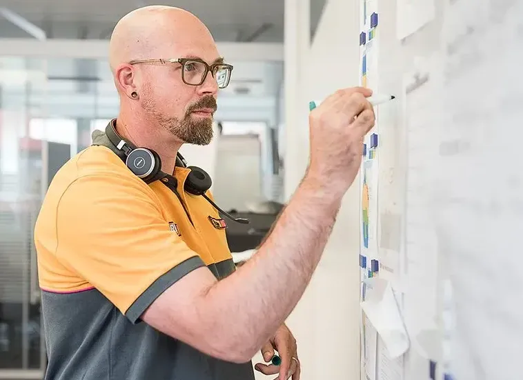 Ein Mitarbeiter von HORNBACH in Arbeitskleidung schreibt Notizen auf ein Whiteboard in einem Büro.