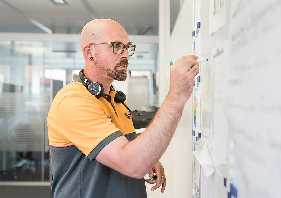 Ein Mitarbeiter von HORNBACH Baumarkt AG schreibt Notizen auf ein Whiteboard in einem modernen Büro.