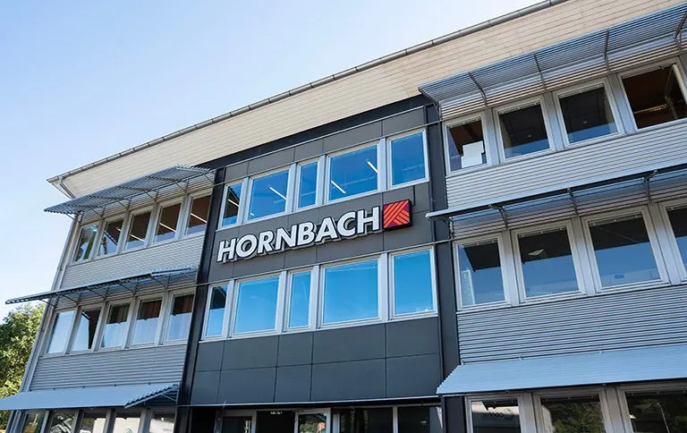 Byggnad med Hornbachs skylt och flaggor vajande utanför, en solig dag. Perfekt för dig som gillar att jobba inom detaljhandeln!