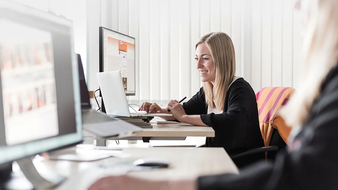 Eine Frau arbeitet lächelnd an einem Computer in einem Büro, ideal für eine Karriere bei HORNBACH Baumarkt AG im Einzelhandel.