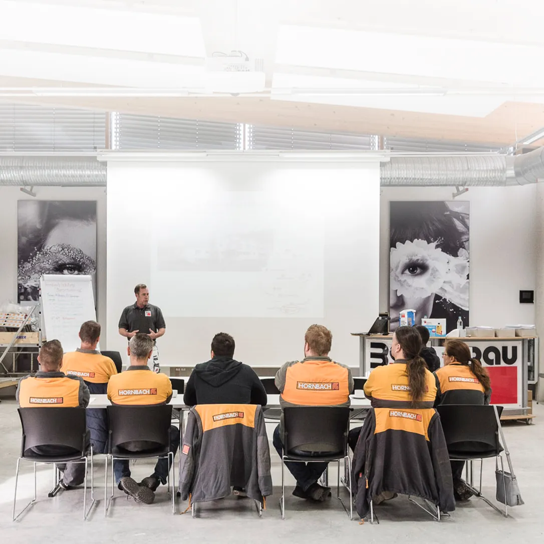 Mitarbeiterschulung bei HORNBACH Baumarkt AG: Ein Trainer erklärt einer Gruppe von Mitarbeitern im Konferenzraum ein Konzept.