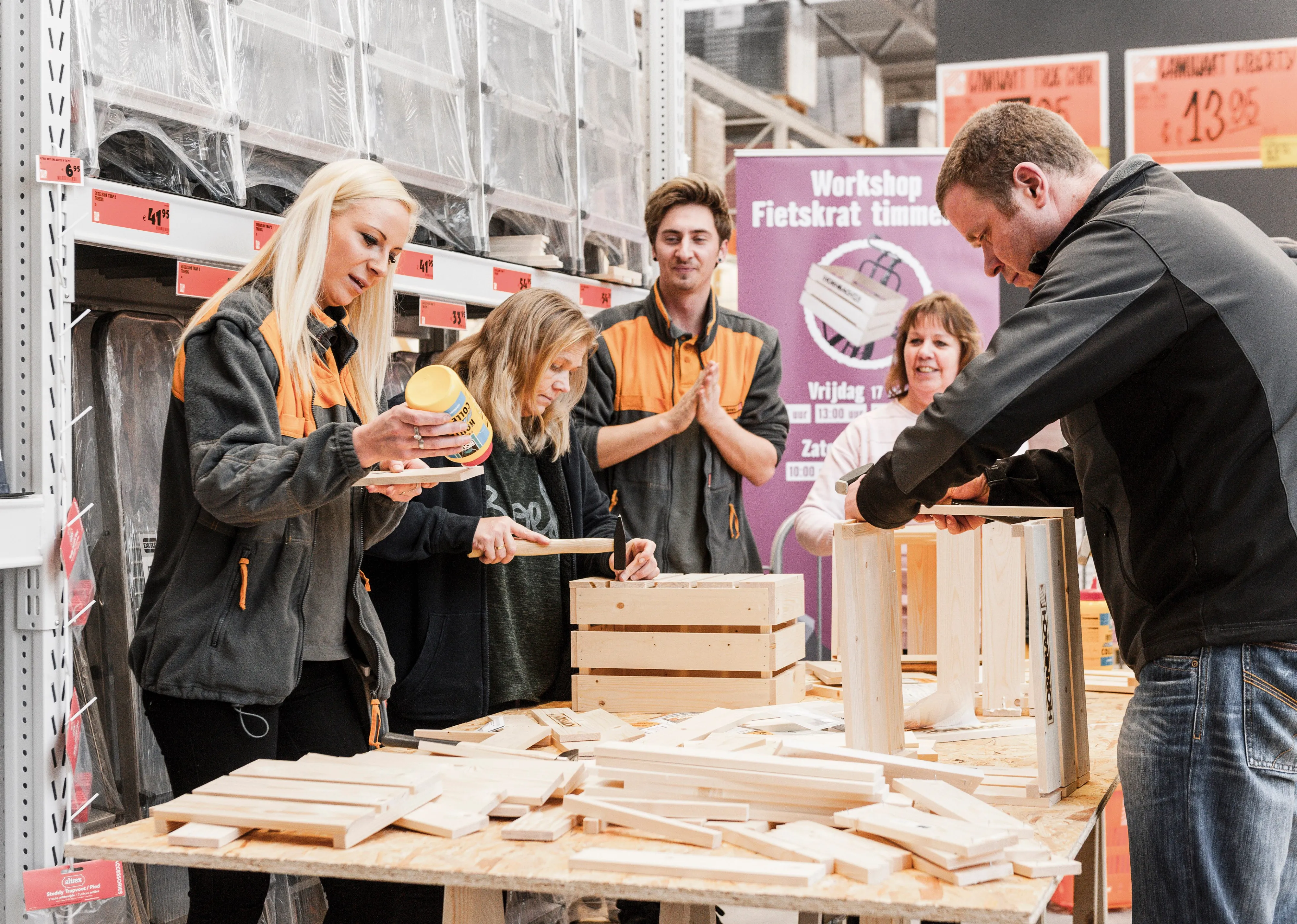 Mitarbeiter von HORNBACH leiten einen Holzbau-Workshop im Baumarkt. Teilnehmer arbeiten an Holzkisten.
