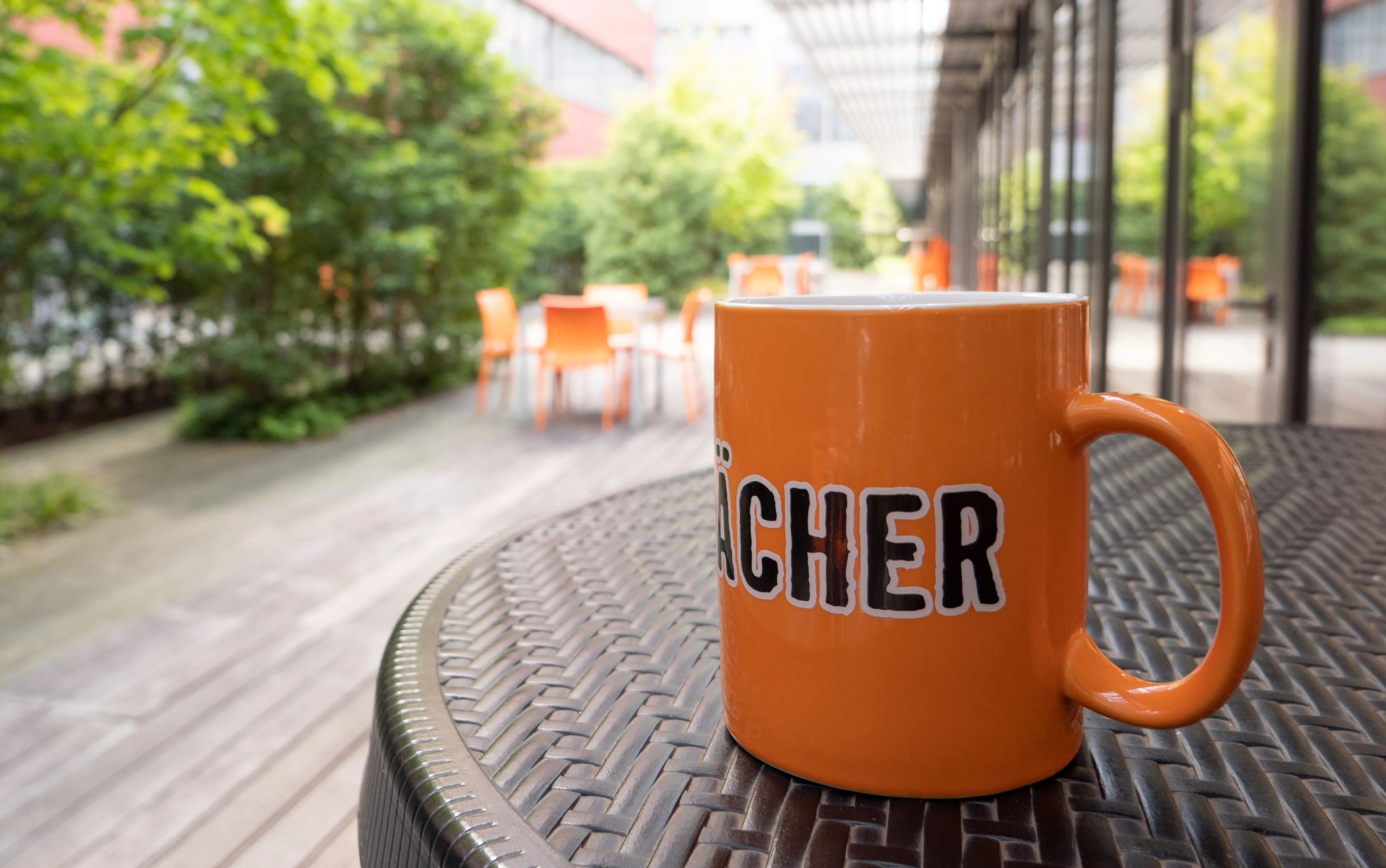 Eine orange Tasse mit Aufschrift steht auf einem Tisch in einem sonnigen Außenbereich von HORNBACH Baumarkt AG.