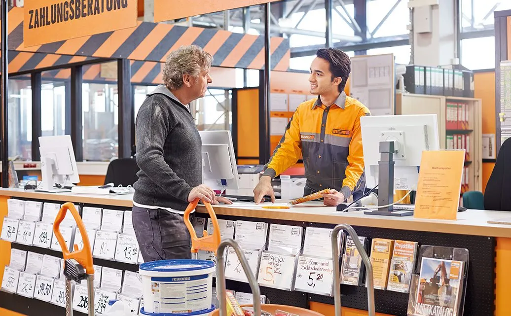 Ein Mitarbeiter von HORNBACH Baumarkt AG berät einen Kunden am Zahlungsberatungs-Schalter in einer Filiale.