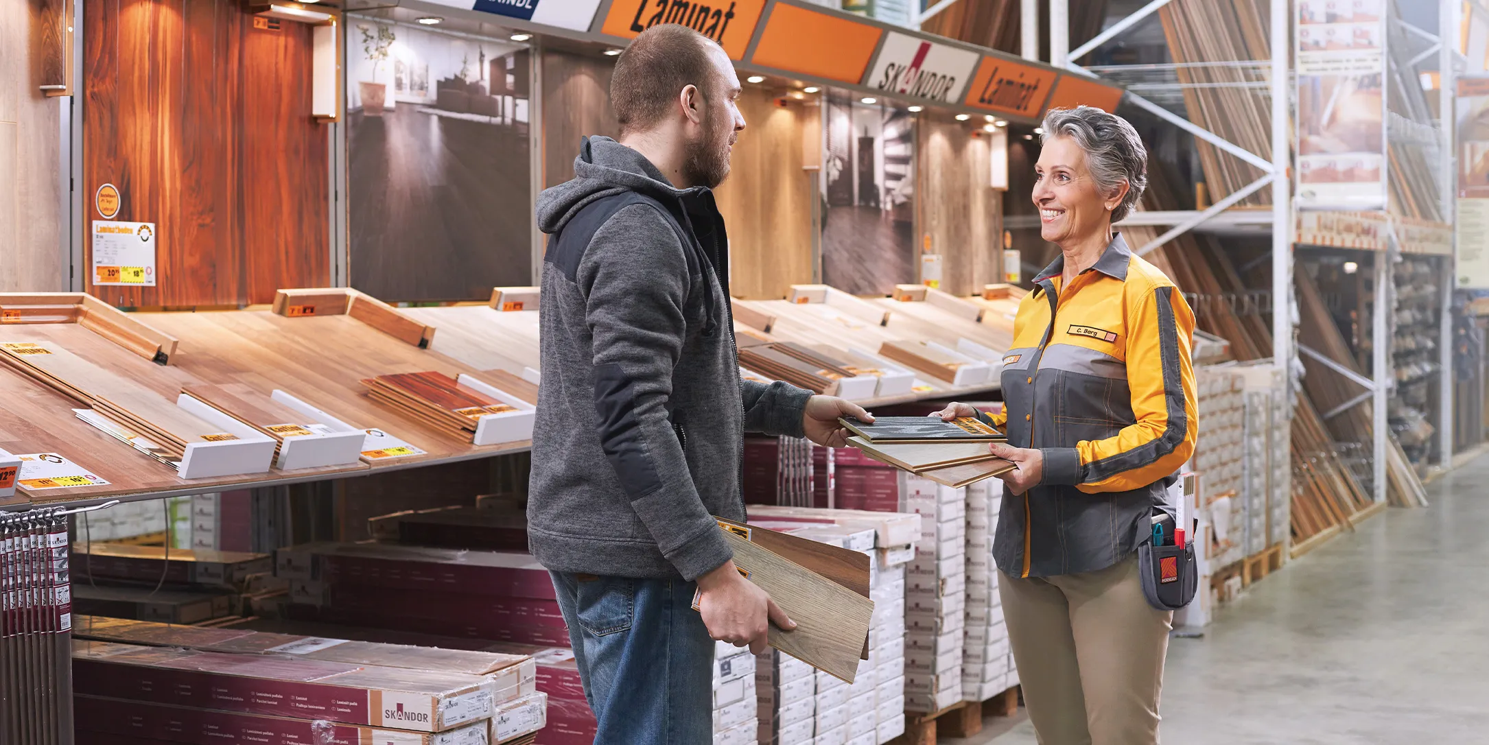 Un client discute avec une employée souriante chez HORNBACH, entouré de matériaux de revêtement de sol.