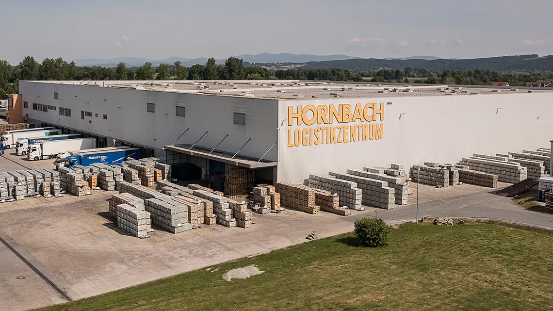 Luftaufnahme des HORNBACH Logistikzentrums mit LKWs und gestapelten Baumaterialien auf dem Gelände.