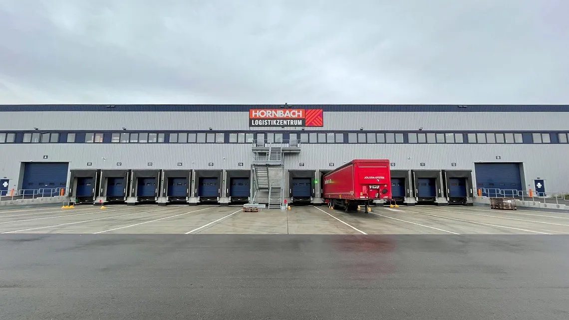 Ein modernes Logistikzentrum von HORNBACH mit mehreren Laderampen und einem roten LKW auf dem Parkplatz.