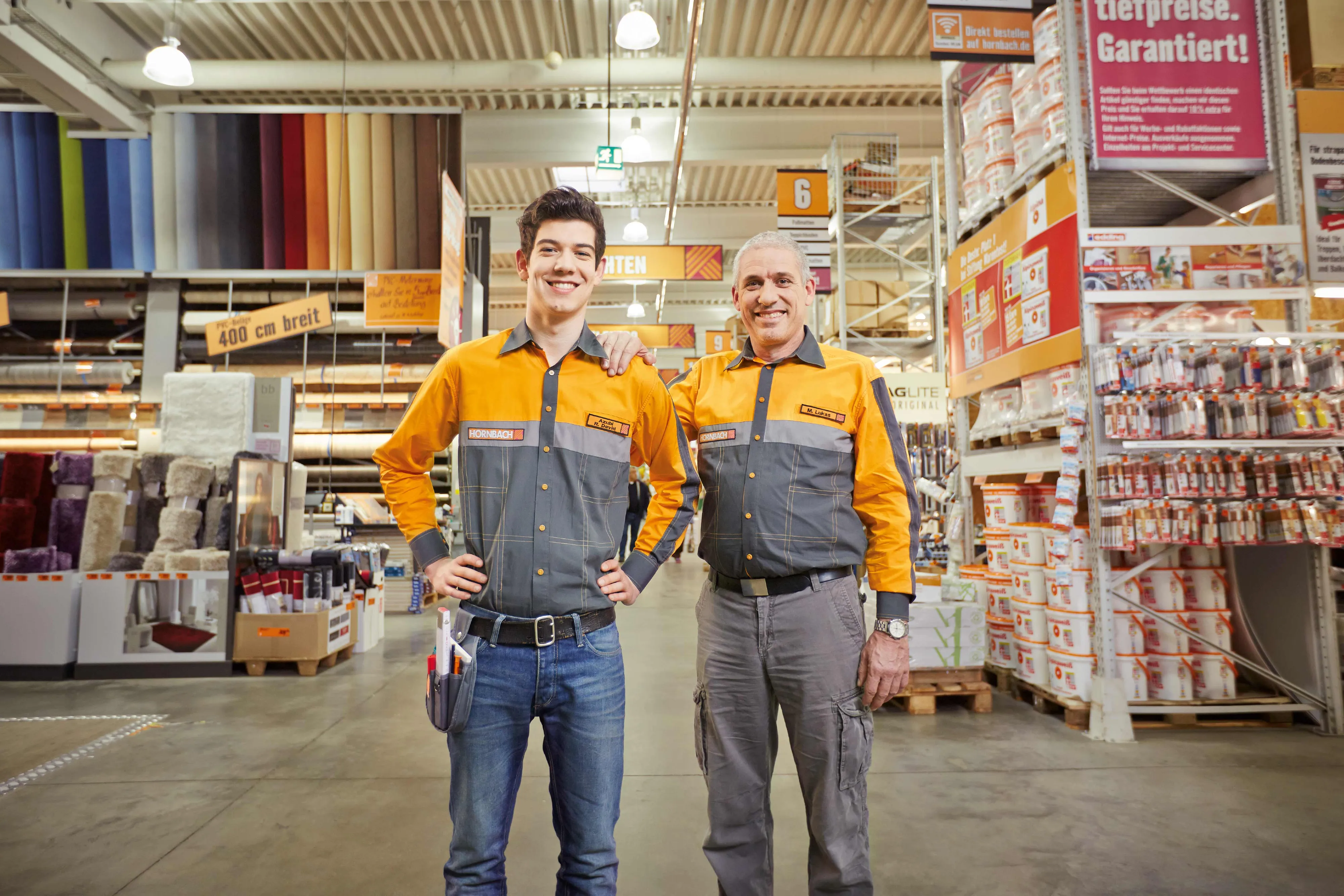 Deux employés souriants de HORNBACH Baumarkt AG posent dans un magasin, entourés de produits de bricolage et de décoration.