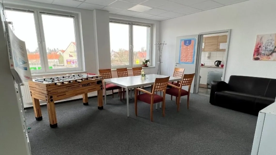 Heller Pausenraum mit Tischkicker, Esstisch, Stühlen und Sofa im Büro von impeak GmbH für Deine entspannte Auszeit.