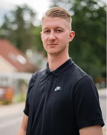 Junger Mann im schwarzen Polohemd blickt selbstbewusst in die Kamera, ideal für Deinen Karrierestart bei impeak GmbH.