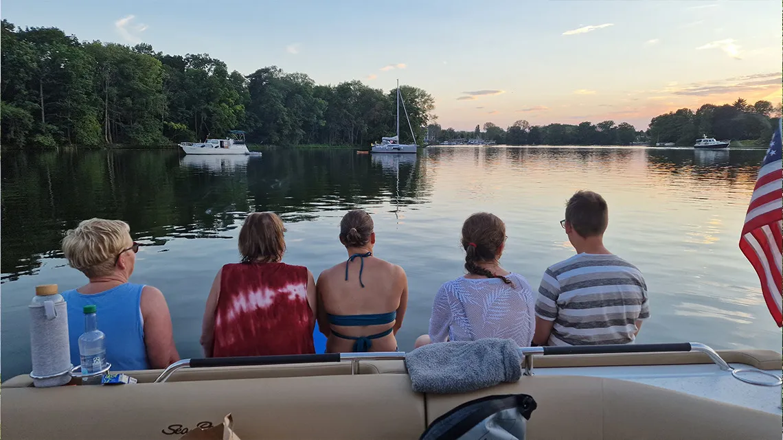 Fünf Personen sitzen gemeinsam auf einem Boot und genießen den Sonnenuntergang auf einem ruhigen See – Teamgefühl bei impeak.