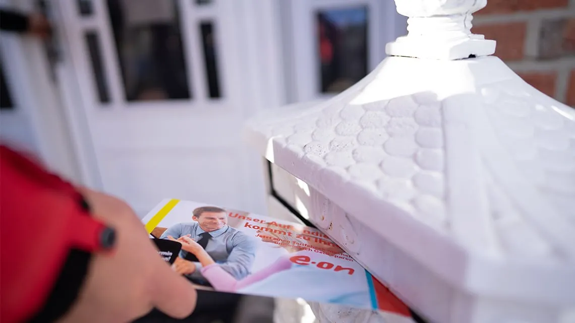 Eine Hand wirft einen Beratungsflyer von impeak GmbH in einen weißen Briefkasten vor einer Haustür ein.