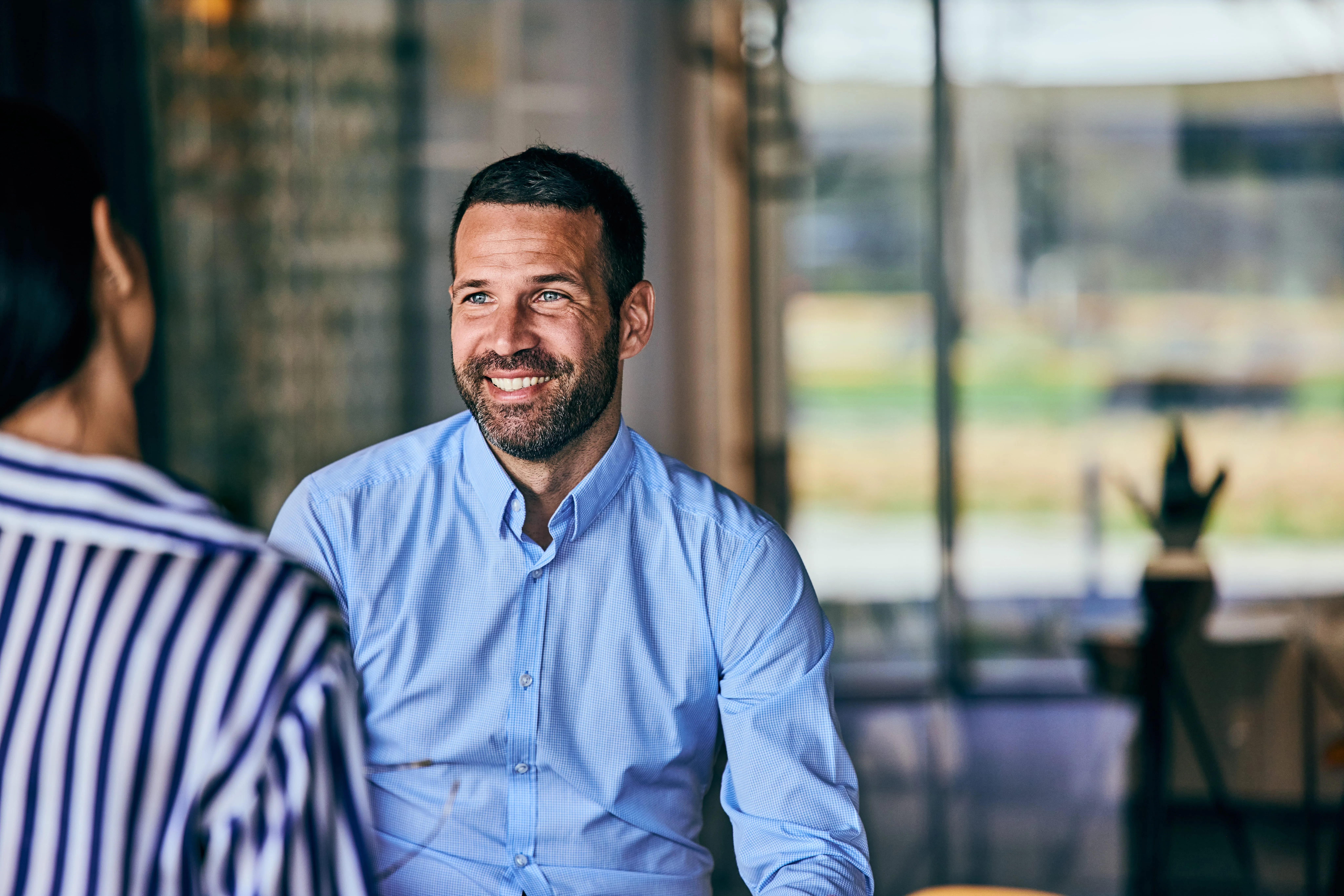 Ein lächelnder Mann im Gespräch mit einer Kollegin in einem modernen Büro von Interhyp AG.