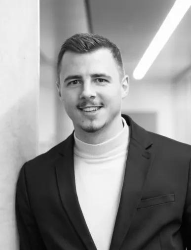 Junger Mann im Anzug lächelt freundlich in einer modernen Büroumgebung – Deine Karriere bei Interhyp AG.