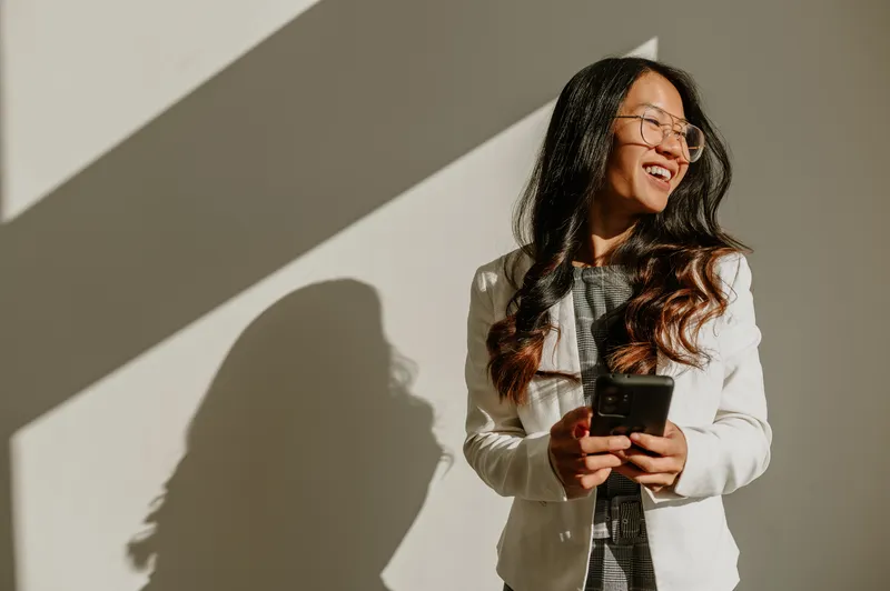 Junge Frau im Business-Outfit lächelt und hält ein Smartphone in der Hand, ideales Motiv für Deine Karriere bei Interhyp.