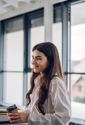 Junge Frau mit Kaffeebecher lächelt entspannt in einem modernen Büro bei Interhyp AG.