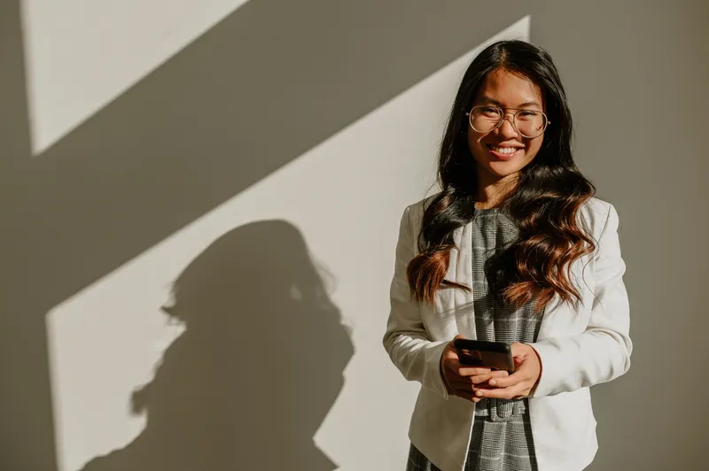Junge Frau im Business-Outfit lächelt und hält ein Smartphone, ideales Arbeitsumfeld für Deine Karriere bei Interhyp AG.