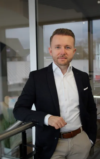 Ein junger Mann im Business-Outfit lehnt entspannt am Treppengeländer im modernen Büro von Interhyp AG.