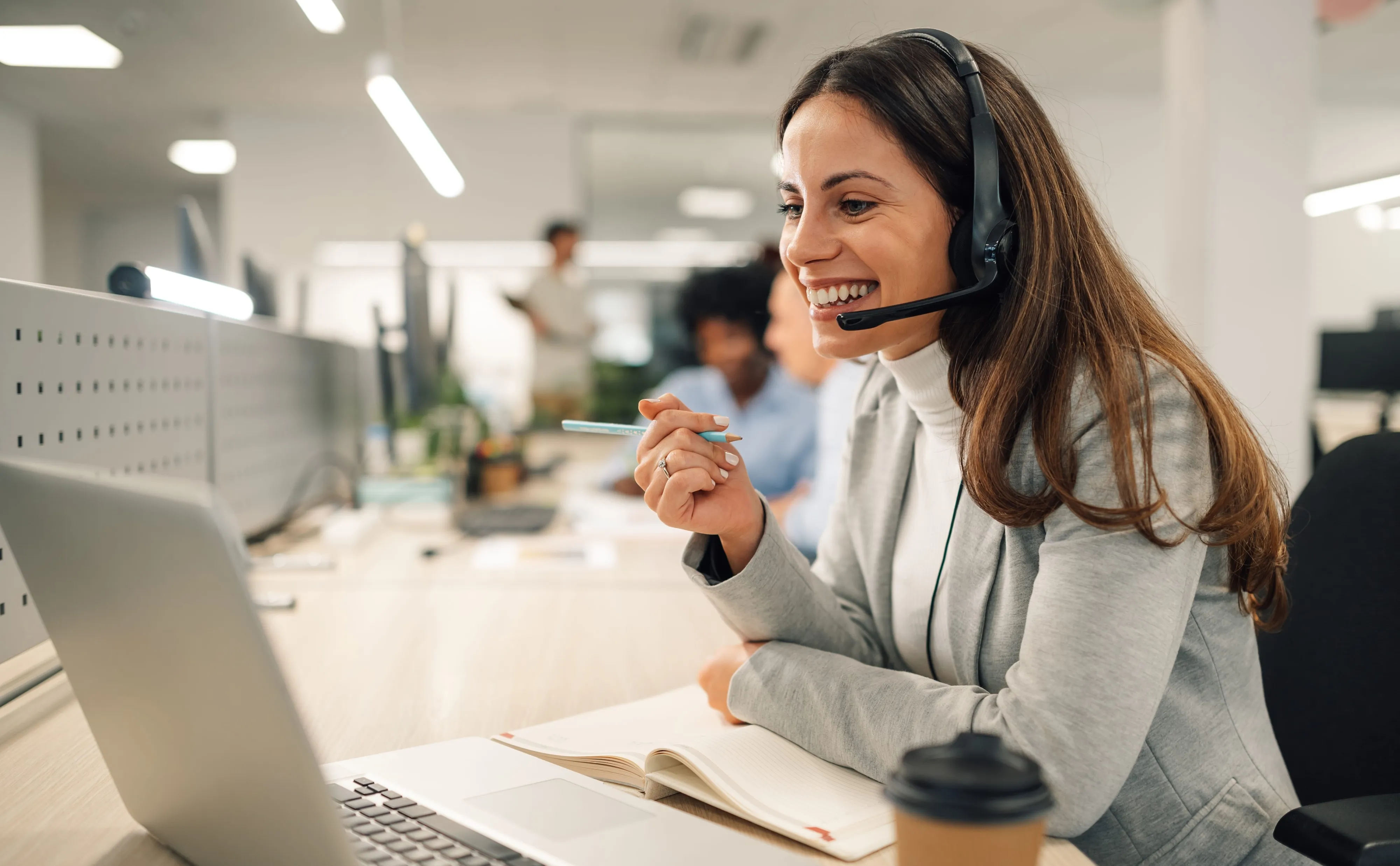 Eine lächelnde Frau mit Headset arbeitet an einem Laptop in einem modernen Büro bei Interhyp AG im Finanzsektor.