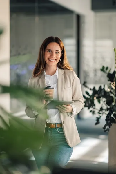 Junge Frau im modernen Büro mit Kaffeebecher und Tablet, bereit für Deinen Karrierestart bei Interhyp AG im Finanzbereich.