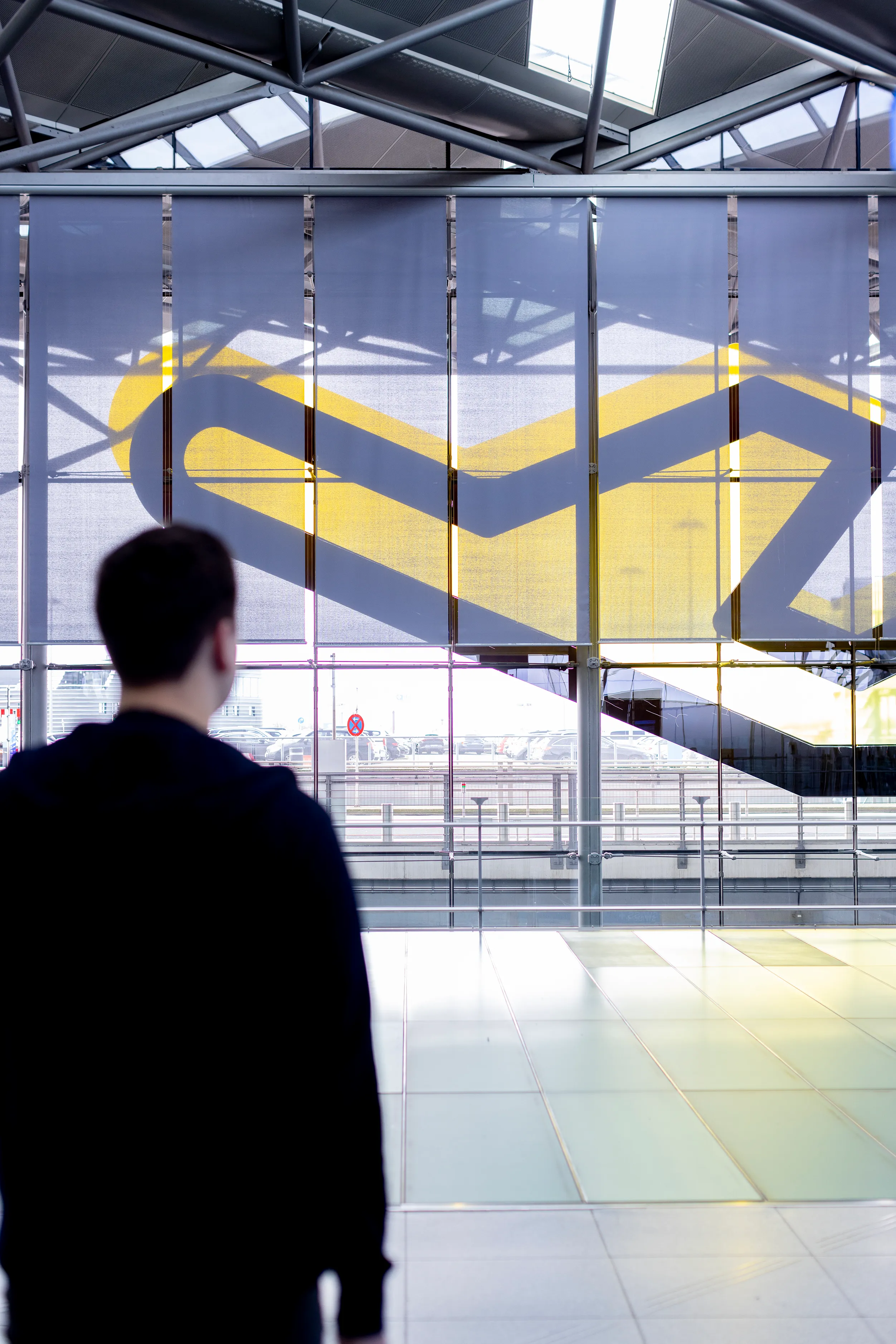 Ein Mann steht in einem modernen, lichtdurchfluteten Gebäude und schaut auf ein großes Fenster mit gelbem Muster.