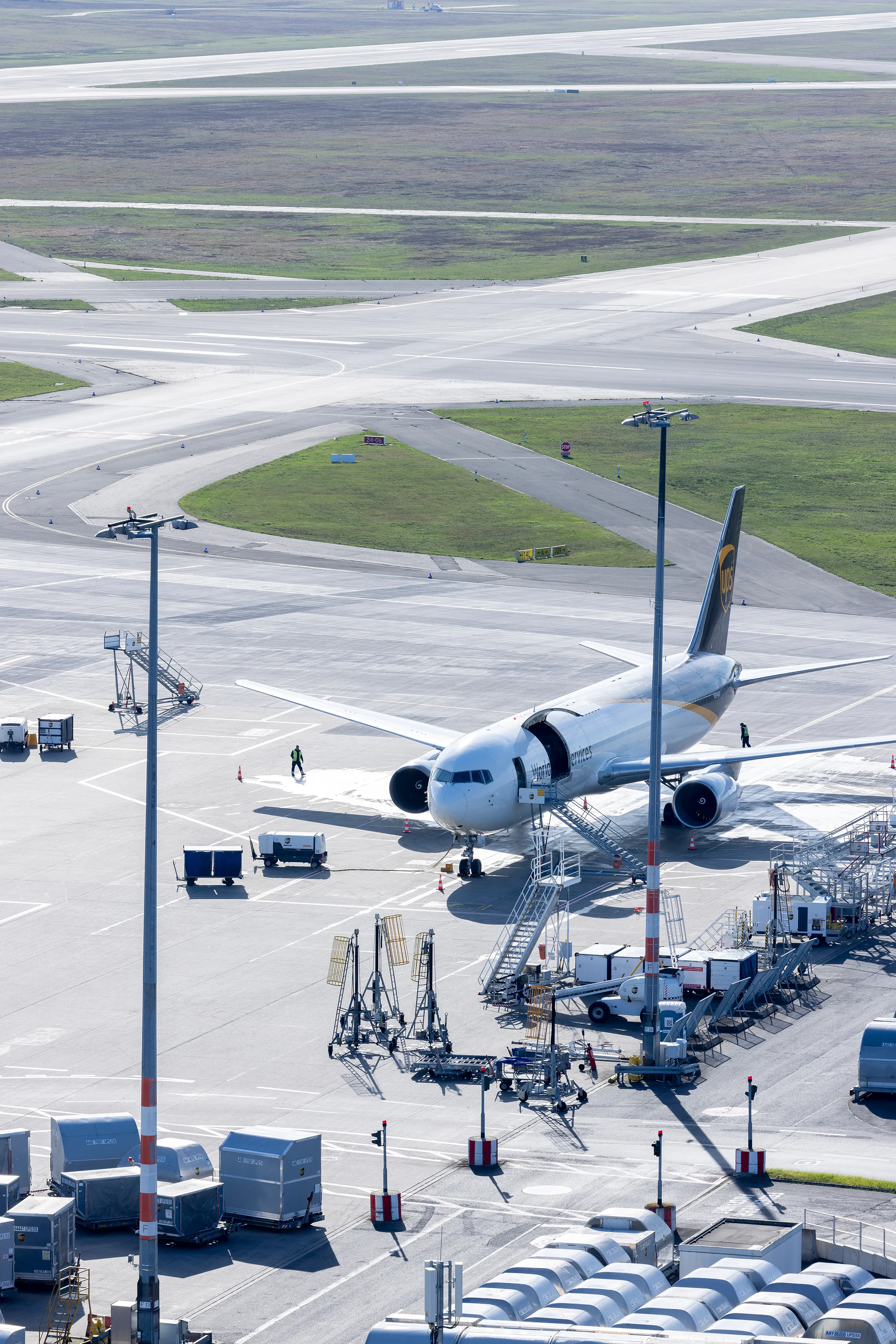 Ein Frachtflugzeug steht auf dem Rollfeld eines Flughafens, umgeben von Ladeausrüstung und Containern.