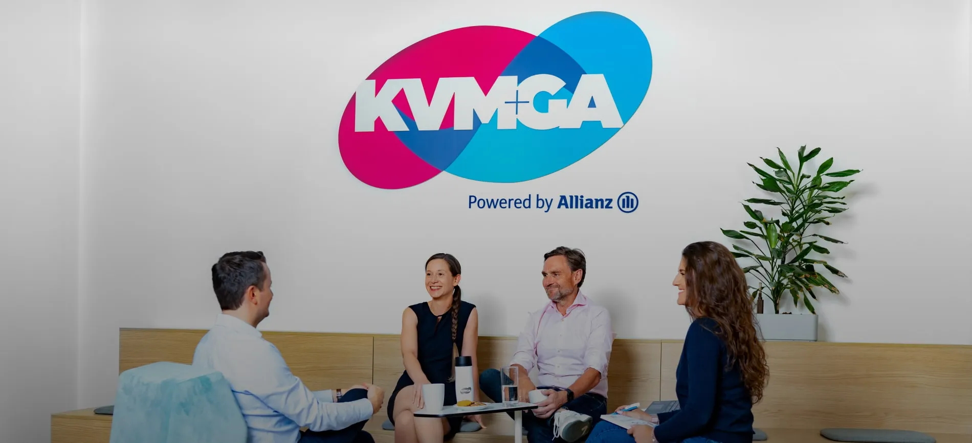 Vier Kollegen unterhalten sich entspannt in der KVM ServicePlus Lounge, das Firmenlogo im Hintergrund.
