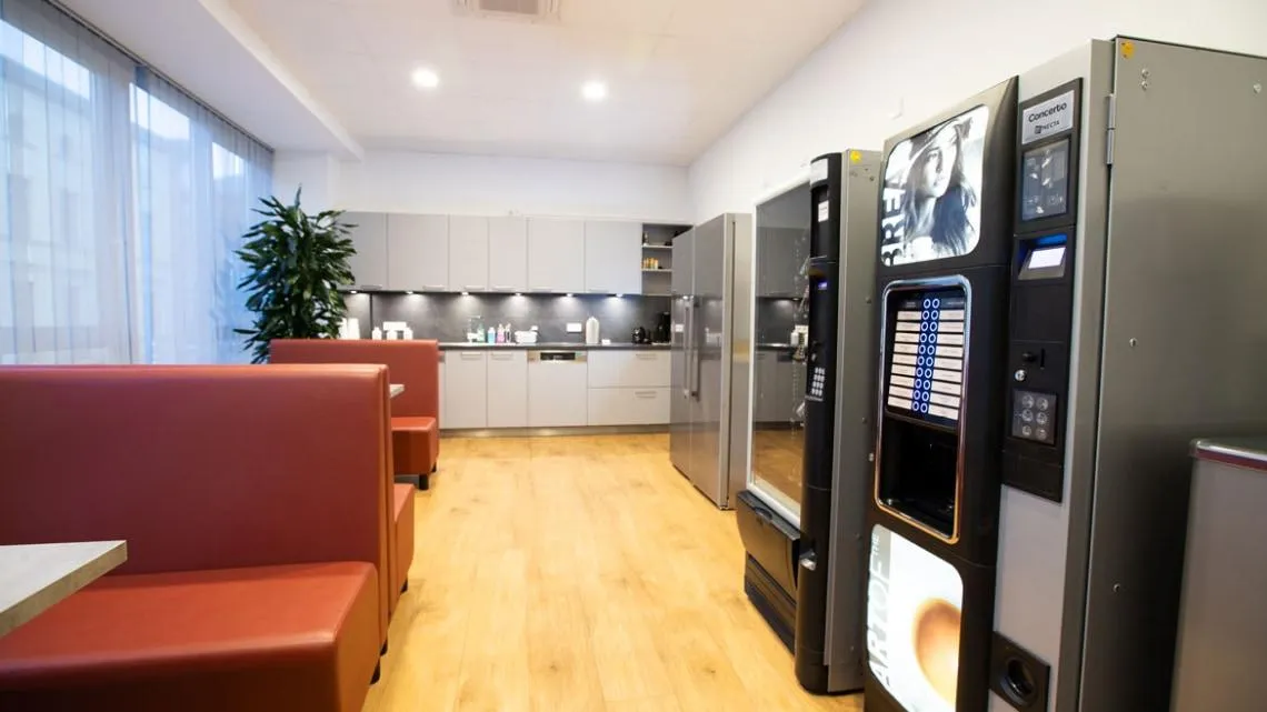 Moderne Kaffeeküche mit roten Sitzbänken, Snackautomaten und großzügiger Küchenzeile für Deine Pausen bei KVM ServicePlus.
