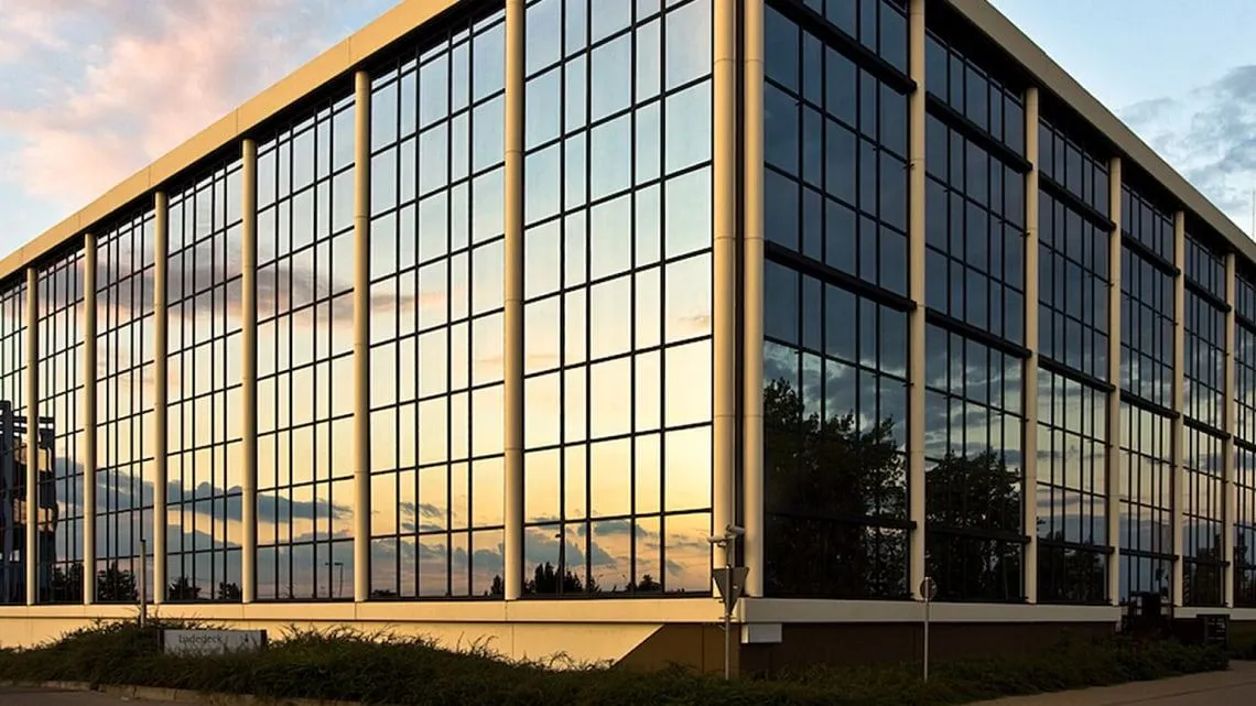 Modernes Bürogebäude von KVM ServicePlus mit Glasfassade bei Sonnenuntergang – hier kannst Du Deine Karriere starten.