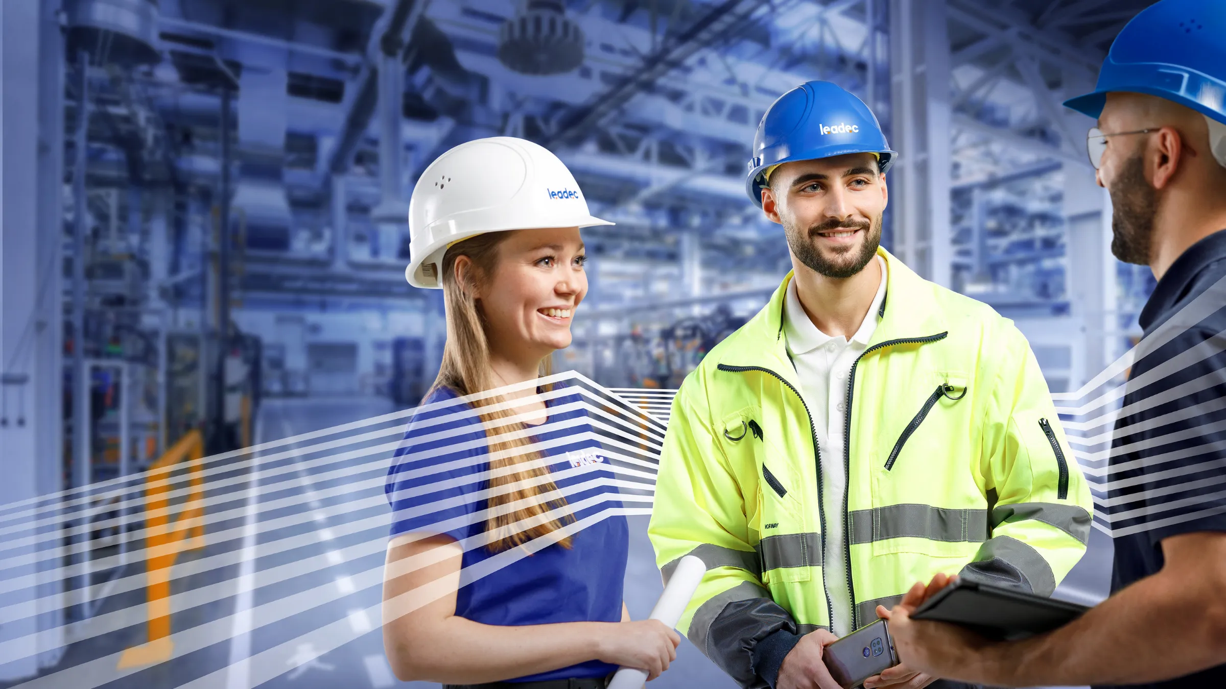 Drei Leadec-Mitarbeitende mit Schutzhelmen unterhalten sich freundlich in einer modernen Industriehalle.