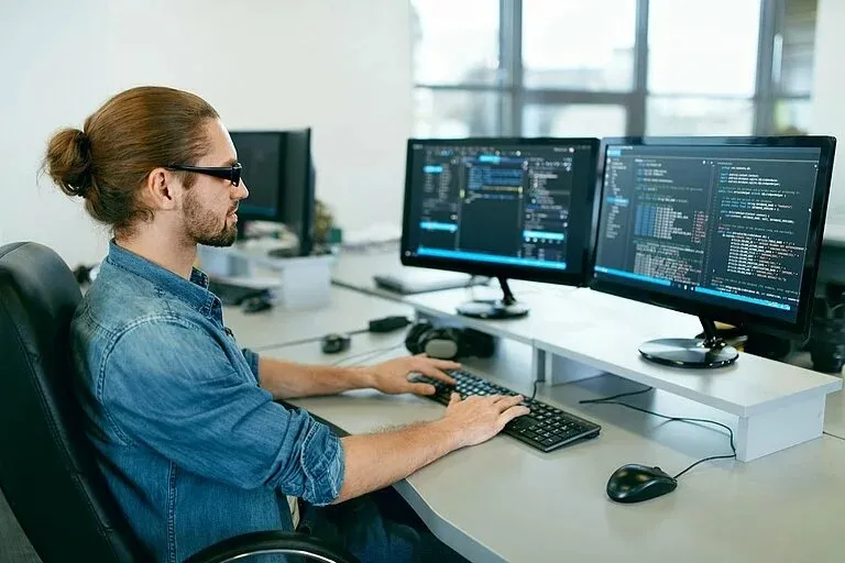 Ein IT-Spezialist arbeitet an zwei Monitoren mit Code in einem modernen Büro – entdecke Deine IT-Karriere bei Leadec.
