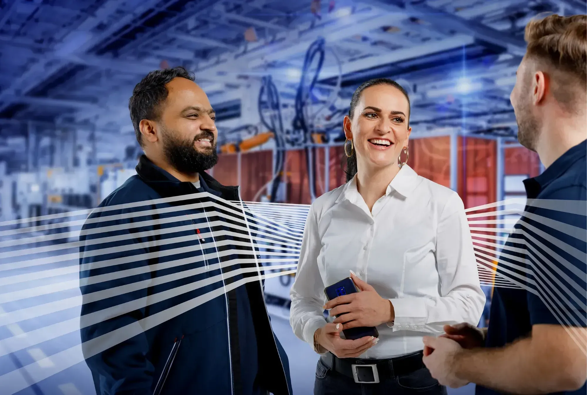 Drei Leadec-Mitarbeiter unterhalten sich lachend in moderner Industrieumgebung – Teamwork und Zusammenarbeit stehen im Fokus.