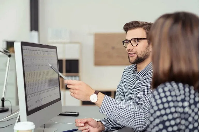 Ein Kollege zeigt Dir am Computer wichtige Projektdaten und erklärt Details in einem modernen Büro.