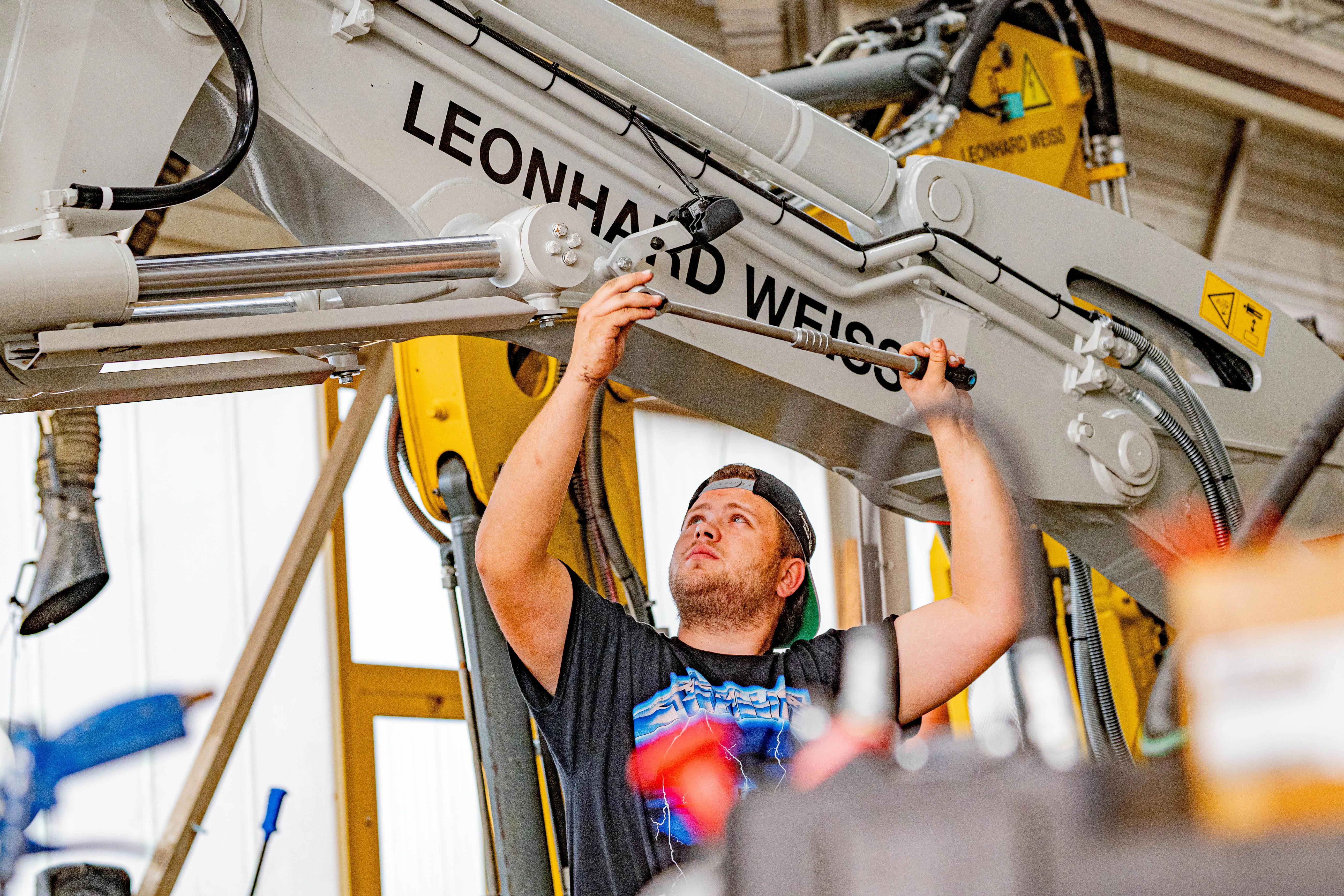 Ein Schweißer mit Schutzhelm arbeitet an einem Metallteil in einer Werkstatt bei Leonhard Weiss GmbH & Co. KG.