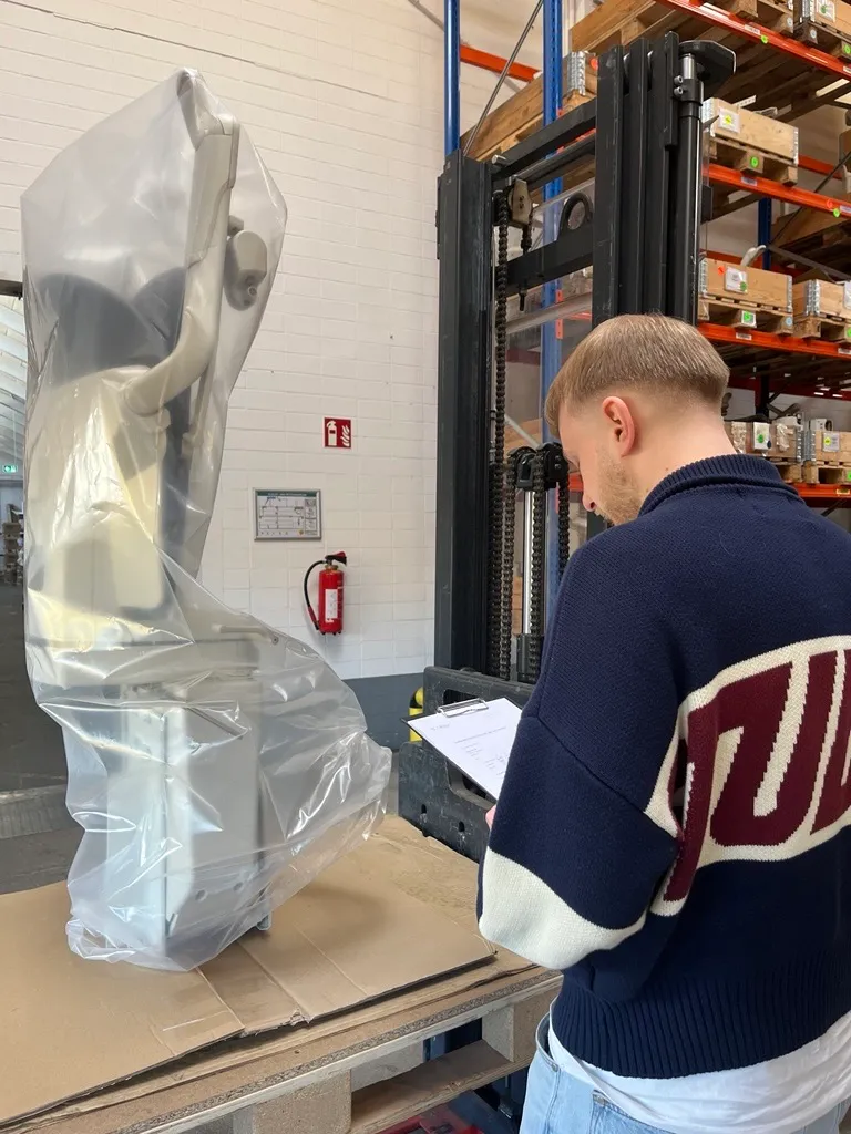 Ein junger Mitarbeiter prüft einen verpackten Treppenlift im Lager von Liftstar GmbH Köln und notiert Details auf einem Klemmbrett.