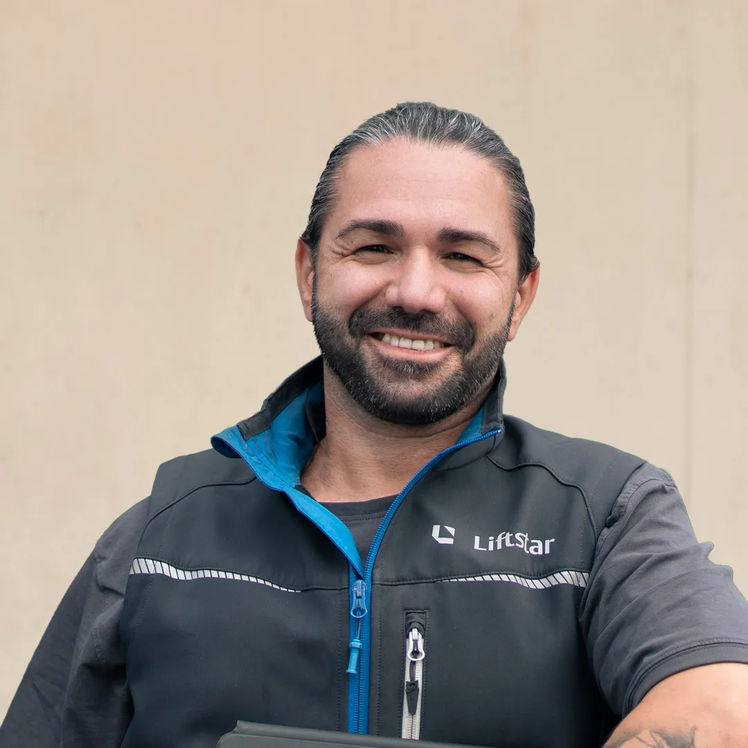 Ein freundlicher Mitarbeiter von Liftstar lächelt Dich an und trägt eine Arbeitsweste mit Firmenlogo.