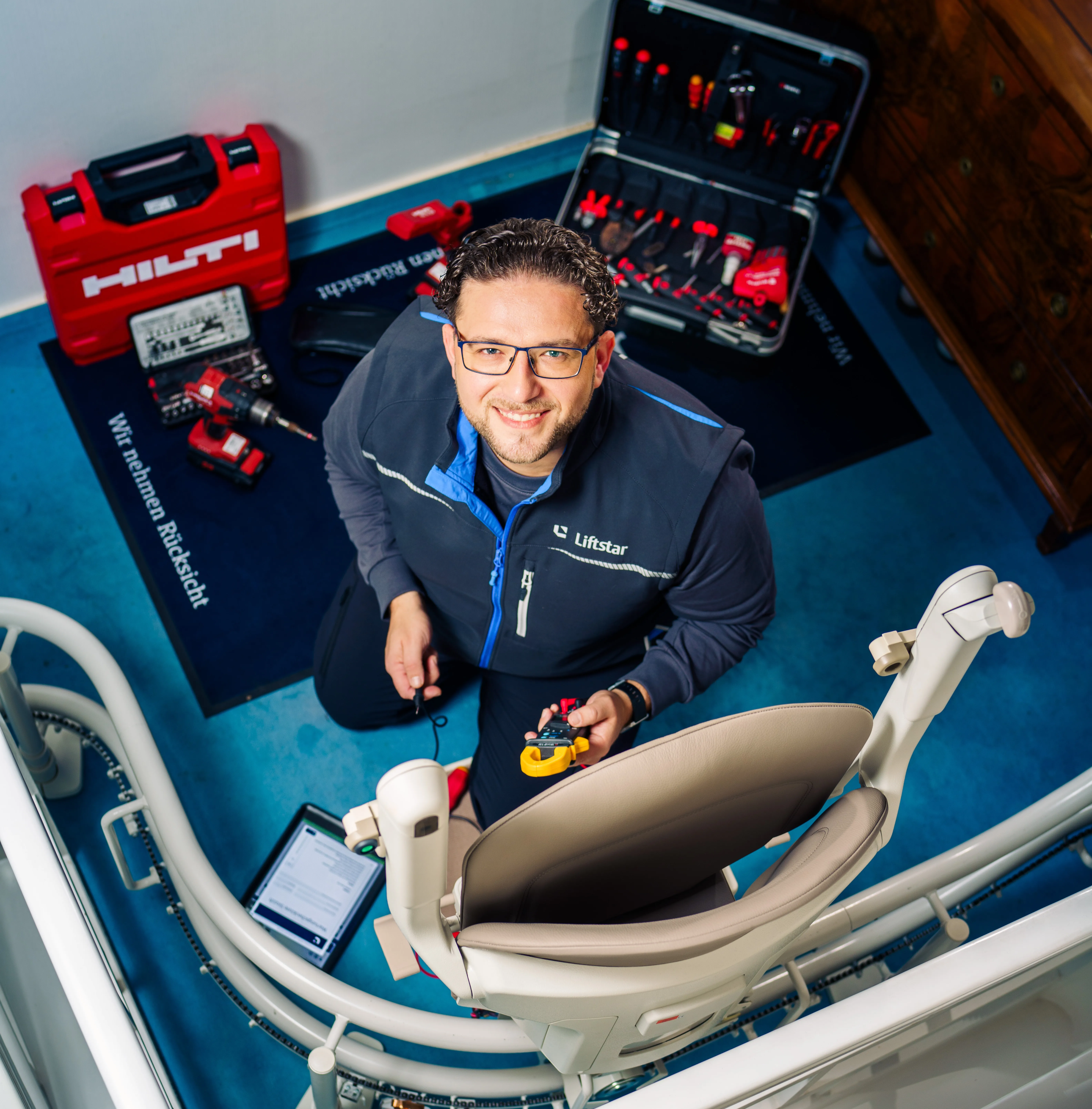 Ein Techniker von Liftstar wartet einen Treppenlift und lächelt, umgeben von Werkzeugen und Arbeitsunterlagen.