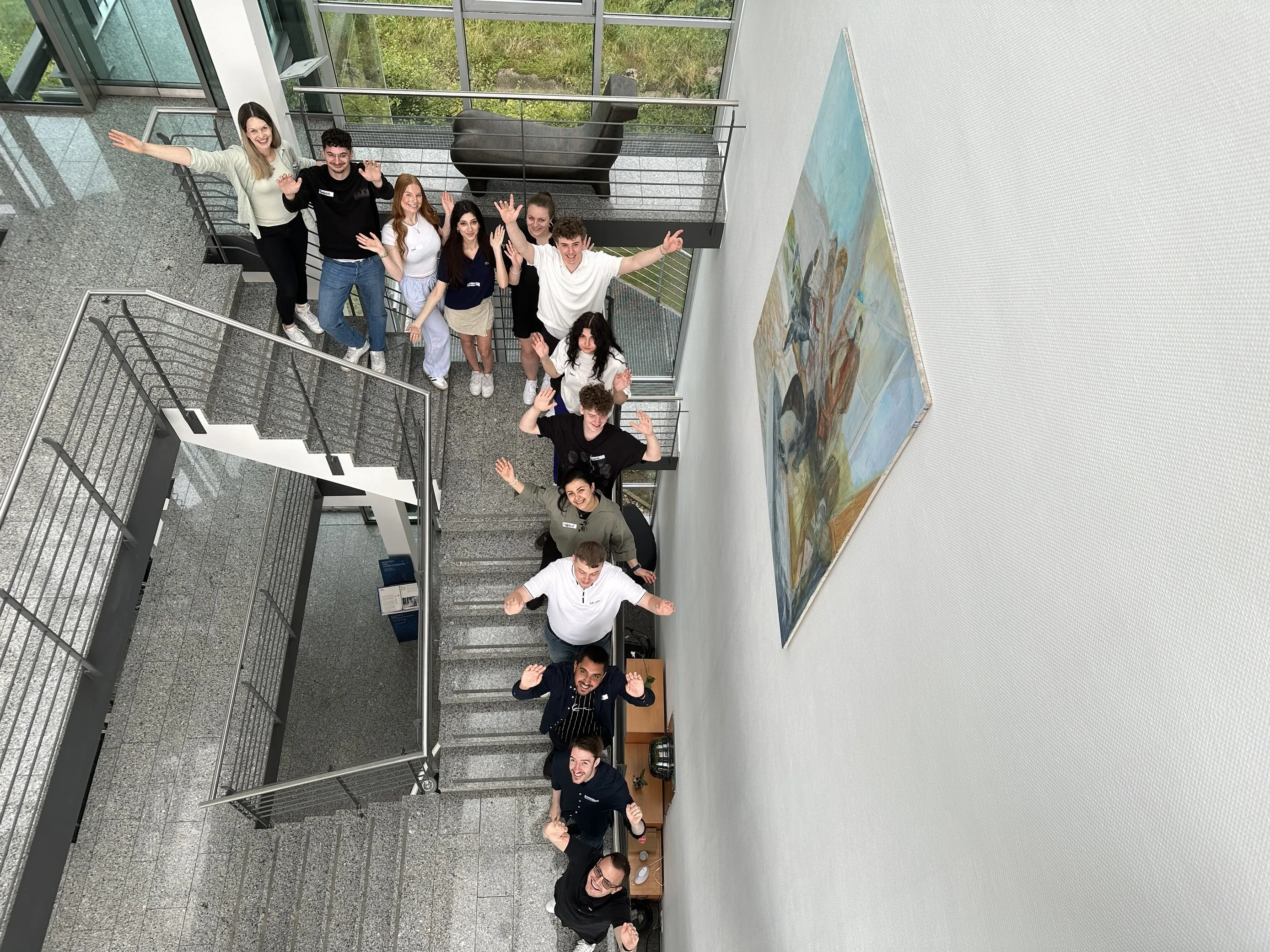 Eine Gruppe junger Kolleginnen und Kollegen von Liftstar begrüßt Dich freundlich auf einer Treppe im modernen Firmengebäude.